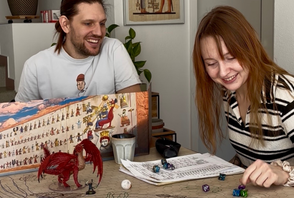 Groupe de joueurs autour d'une table de Donjons et Dragons avec un paravent de MJ, des figurines et des dés