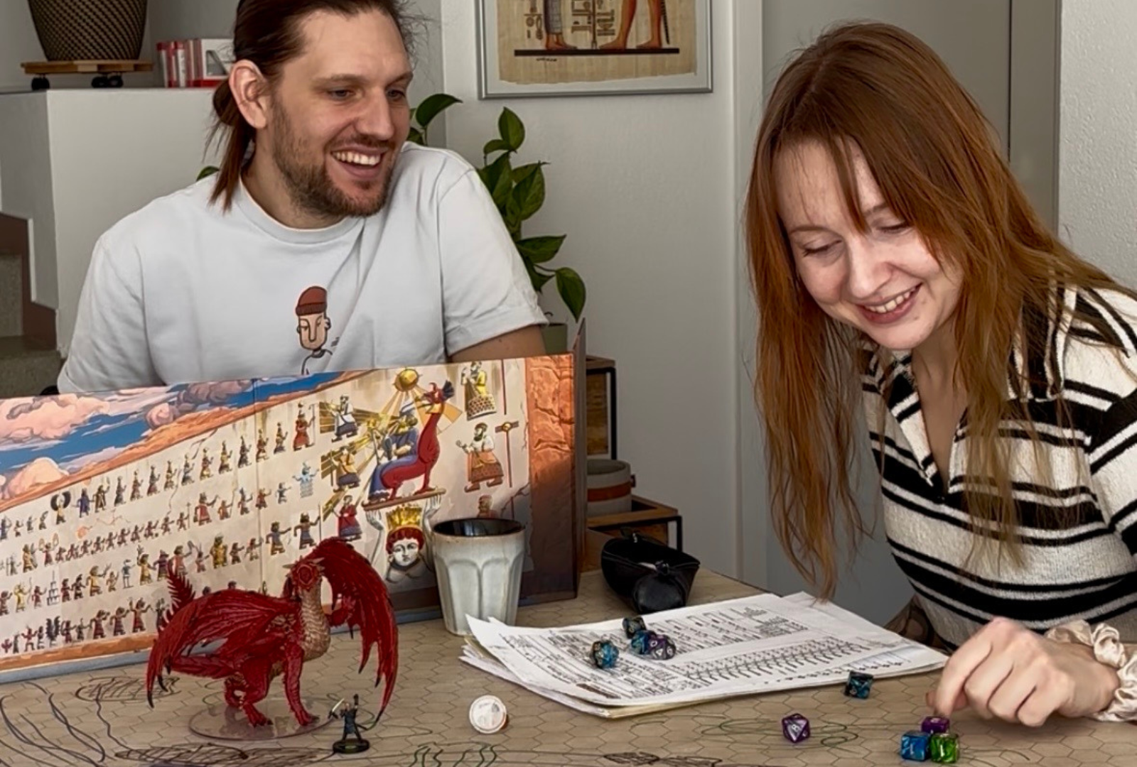 Groupe de joueurs autour d'une table de Donjons et Dragons avec un paravent de MJ, des figurines et des dés